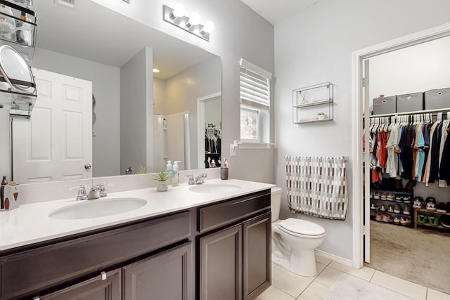 bathroom with a walk in closet, a sink, toilet, and tile patterned floors