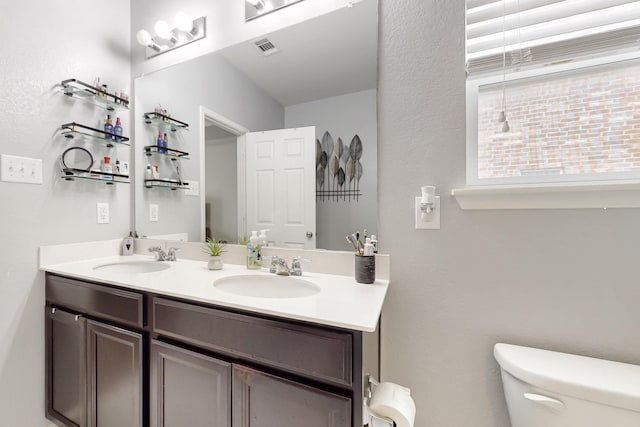 full bathroom featuring toilet, double vanity, visible vents, and a sink