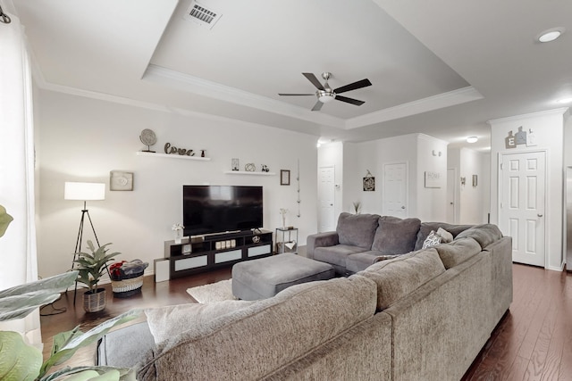 living area with dark wood-type flooring, a tray ceiling, visible vents, and crown molding