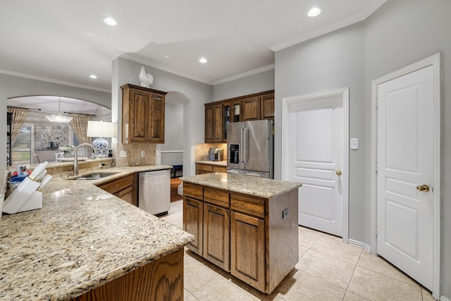 kitchen featuring arched walkways, light stone counters, a sink, appliances with stainless steel finishes, and tasteful backsplash