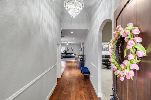 corridor with arched walkways, wood-type flooring, a towering ceiling, and baseboards