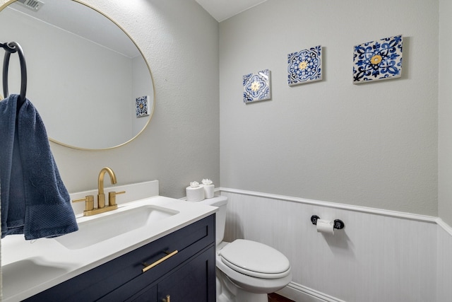 half bathroom with visible vents, wainscoting, vanity, and toilet