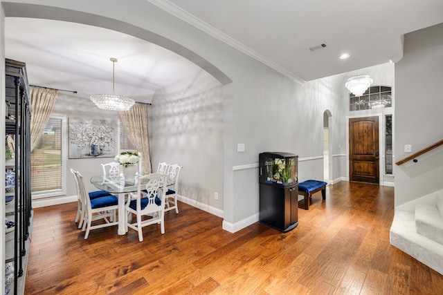 dining room featuring ornamental molding, arched walkways, wood-type flooring, and an inviting chandelier