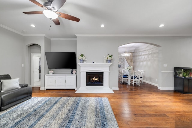 living area featuring baseboards, arched walkways, ornamental molding, wood finished floors, and recessed lighting