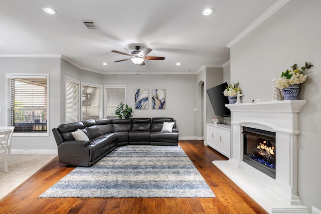 living room featuring a warm lit fireplace, visible vents, crown molding, and baseboards