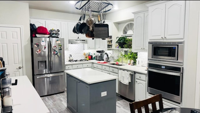 kitchen featuring decorative backsplash, a center island, stainless steel appliances, under cabinet range hood, and a sink