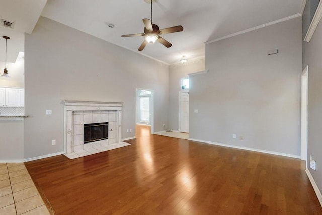 unfurnished living room with baseboards, a ceiling fan, a tile fireplace, wood finished floors, and crown molding