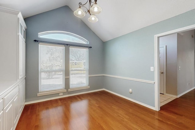 empty room featuring a chandelier, vaulted ceiling, baseboards, and wood finished floors