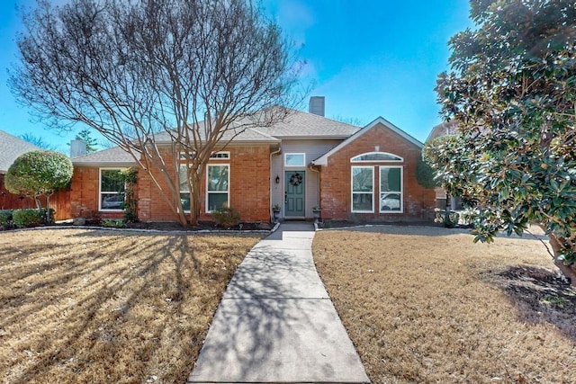 single story home with a shingled roof, a chimney, a front lawn, and brick siding