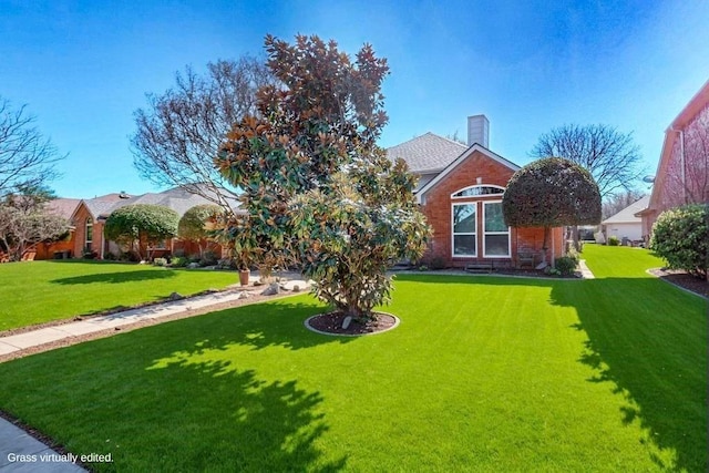 view of front of house featuring a front lawn, a chimney, and brick siding