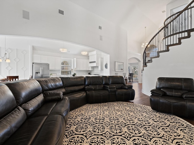 living area featuring arched walkways, dark wood-style flooring, visible vents, a towering ceiling, and stairs