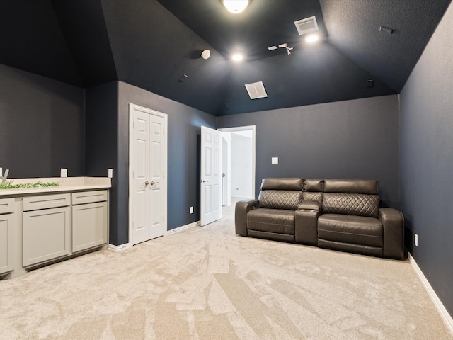 home theater room featuring lofted ceiling, baseboards, visible vents, and light colored carpet