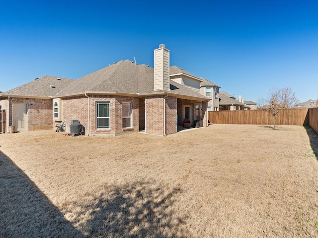 rear view of house with a chimney, brick siding, a fenced backyard, and roof with shingles