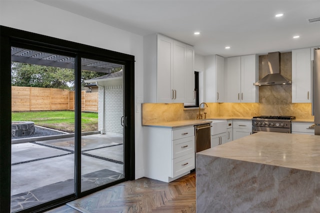 kitchen with light countertops, backsplash, appliances with stainless steel finishes, a sink, and wall chimney range hood