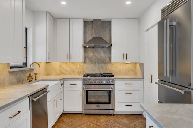 kitchen with wall chimney exhaust hood, high quality appliances, a sink, white cabinetry, and backsplash