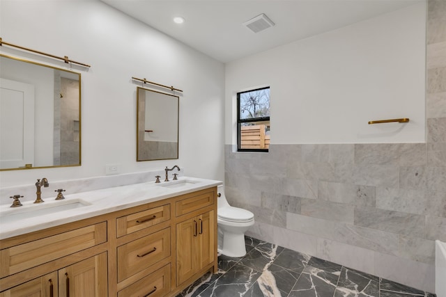 bathroom with toilet, double vanity, a sink, and tile walls