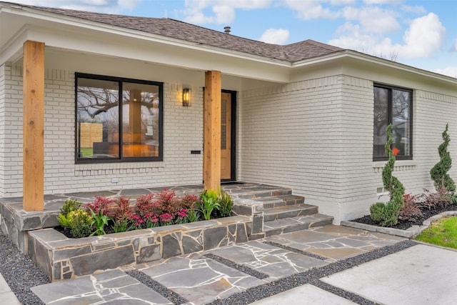 doorway to property with brick siding, roof with shingles, and a porch