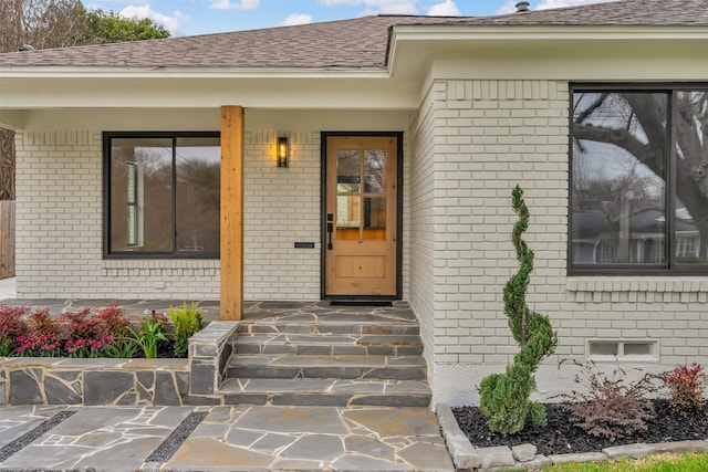 view of exterior entry with crawl space, brick siding, and roof with shingles