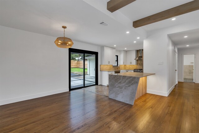 kitchen featuring a peninsula, wall chimney range hood, wood finished floors, and beam ceiling