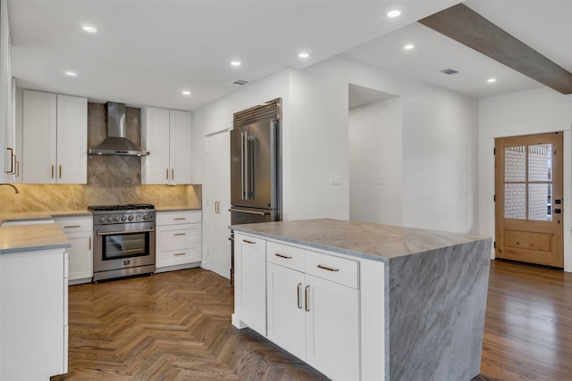 kitchen featuring premium appliances, tasteful backsplash, a kitchen island, a sink, and wall chimney range hood