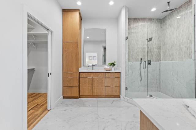 full bath with a walk in closet, marble finish floor, a marble finish shower, recessed lighting, and vanity