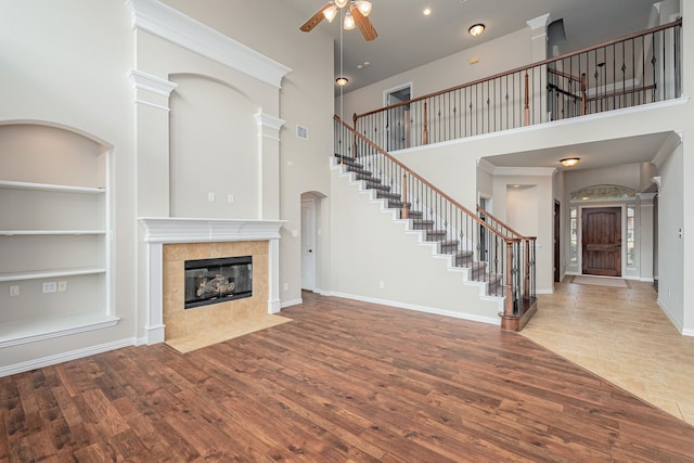 unfurnished living room with built in shelves, stairway, a tiled fireplace, wood finished floors, and baseboards