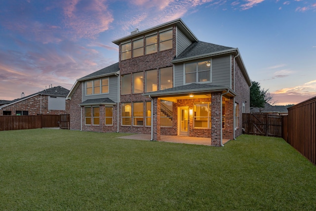 back of house at dusk featuring brick siding, a yard, a fenced backyard, and a patio