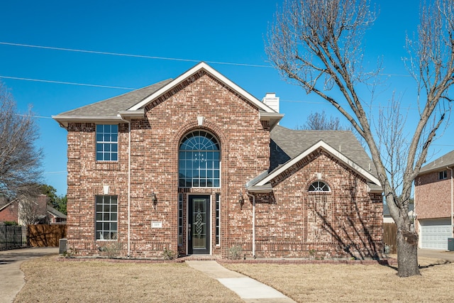 traditional-style home with brick siding, a chimney, a shingled roof, and a front yard