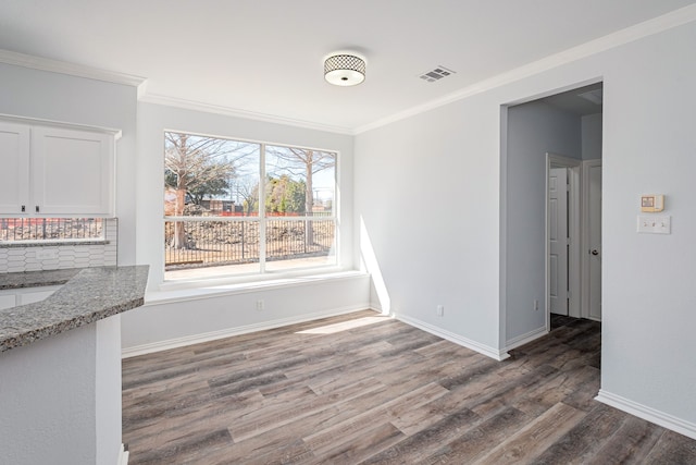 unfurnished dining area with ornamental molding, wood finished floors, visible vents, and baseboards