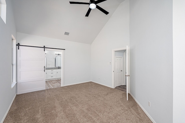 unfurnished bedroom featuring light colored carpet, visible vents, ensuite bathroom, a barn door, and high vaulted ceiling