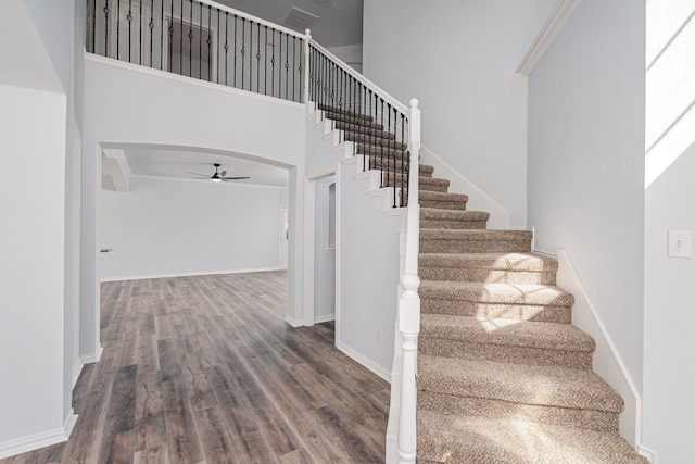 stairway with a towering ceiling, ceiling fan, baseboards, and wood finished floors