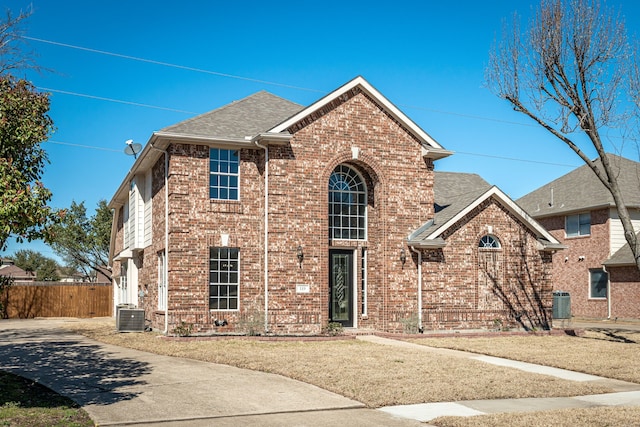 traditional home featuring a shingled roof, fence, central AC unit, and brick siding