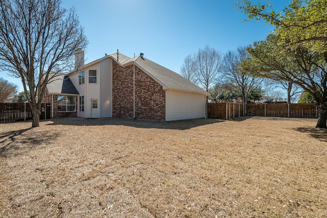 exterior space featuring brick siding, a fenced backyard, a chimney, and a yard