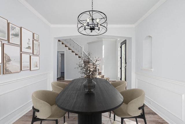 dining room featuring a wainscoted wall, wood finished floors, stairs, ornamental molding, and an inviting chandelier