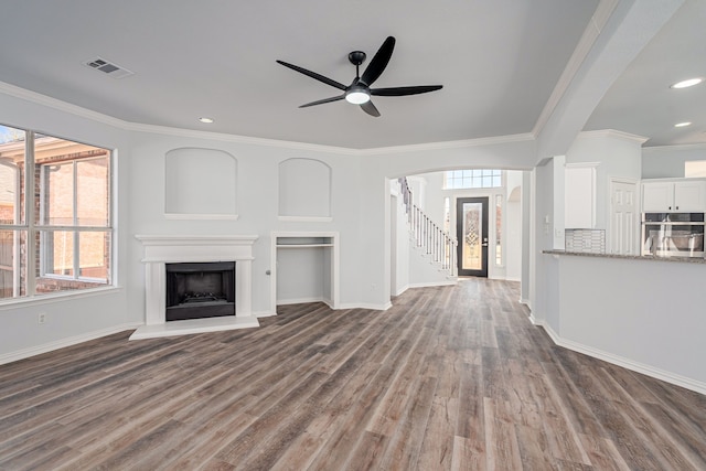 unfurnished living room with a healthy amount of sunlight, visible vents, crown molding, and wood finished floors