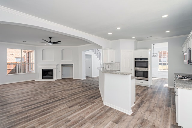 kitchen with appliances with stainless steel finishes, white cabinets, a fireplace with raised hearth, and dark wood-type flooring