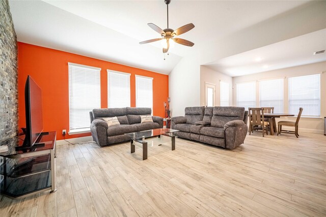 living area featuring visible vents, ceiling fan, vaulted ceiling, light wood-style flooring, and a wood stove