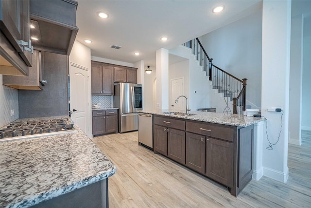 4130 Lagoon Pl, Royse City, TX 75189 - kitchen with stainless steel appliances, a sink, light wood-style floors, decorative backsplash, and dark brown cabinets