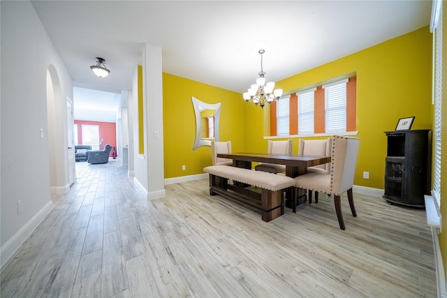 dining room featuring baseboards, a notable chandelier, light wood-style flooring, and arched walkways