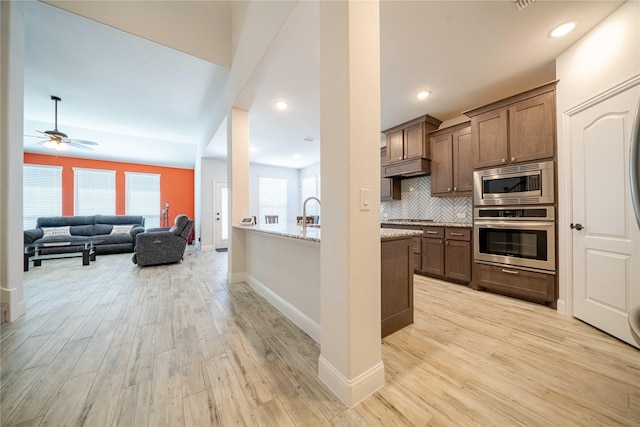 kitchen with tasteful backsplash, light wood finished floors, stainless steel appliances, and light stone countertops