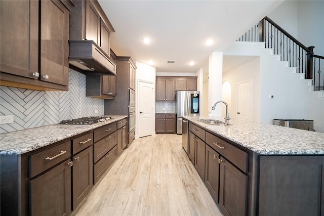 kitchen featuring tasteful backsplash, light wood-type flooring, an island with sink, stainless steel appliances, and a sink