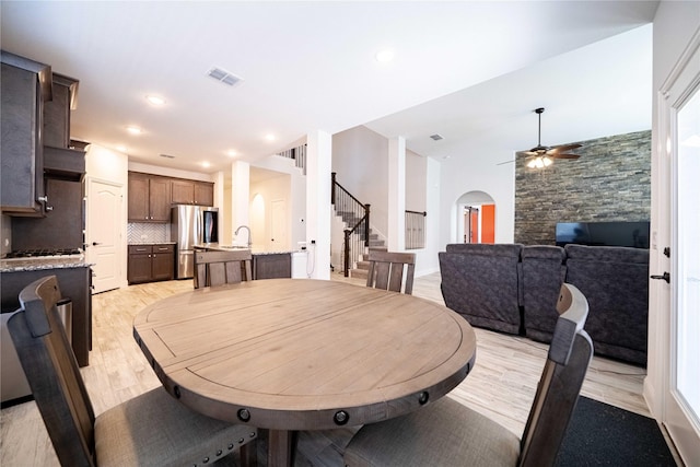 dining space with light wood-type flooring, visible vents, arched walkways, ceiling fan, and stairs