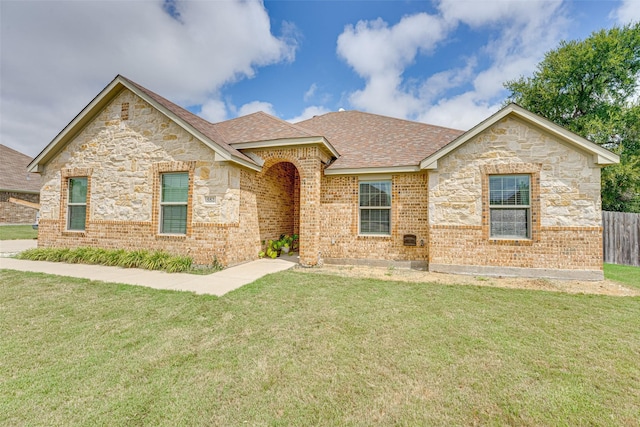 ranch-style home with brick siding, a shingled roof, fence, and a front yard