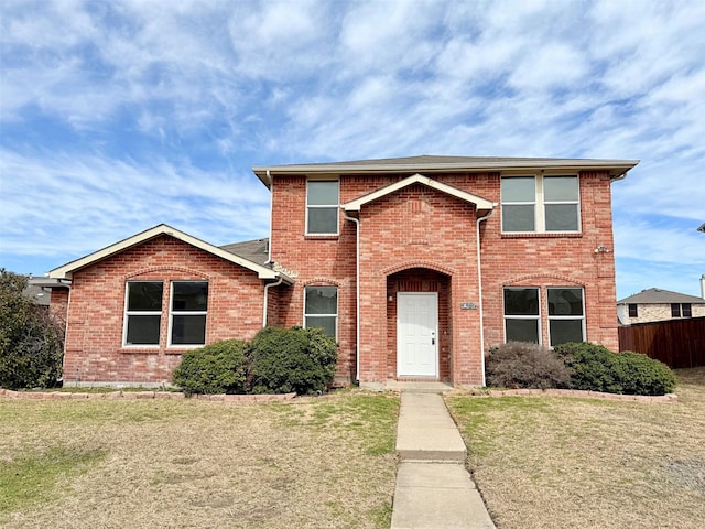 traditional-style house featuring a front yard, brick siding, and fence