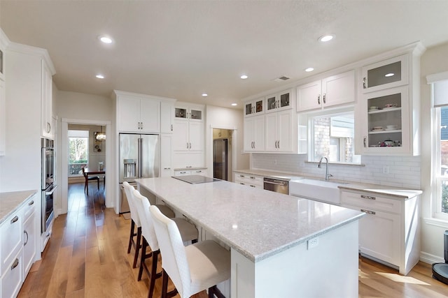 kitchen featuring light wood finished floors, stainless steel appliances, decorative backsplash, a sink, and a kitchen island