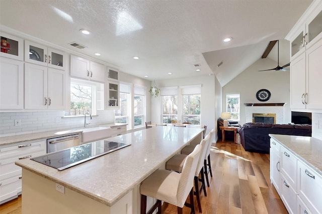 kitchen featuring light wood finished floors, visible vents, black electric stovetop, a brick fireplace, and stainless steel dishwasher