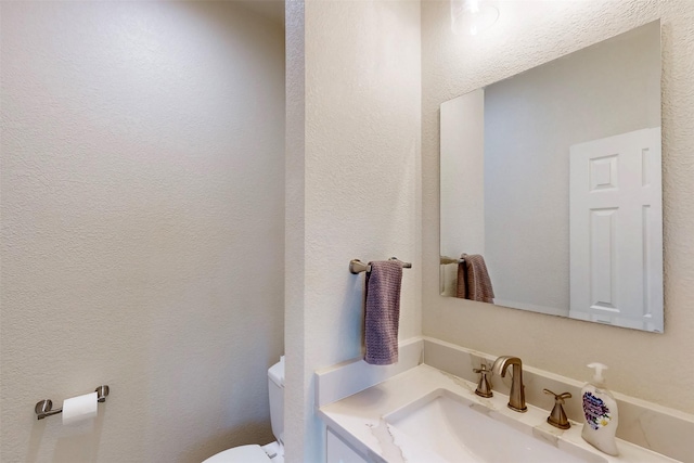 half bath with toilet, a textured wall, and vanity