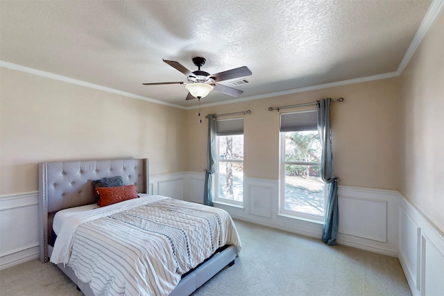 bedroom with a wainscoted wall, visible vents, light carpet, and a textured ceiling