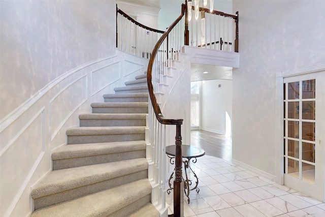 stairs featuring a towering ceiling, a wainscoted wall, and a decorative wall