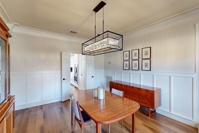 dining room with a wainscoted wall, visible vents, wood finished floors, and ornamental molding